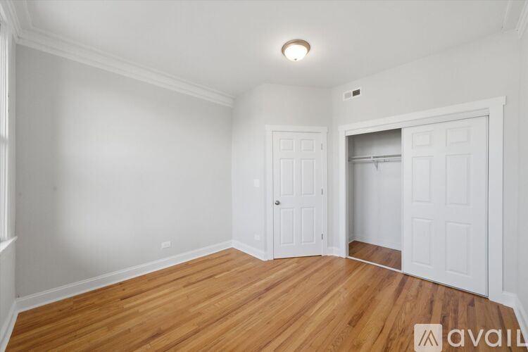 A room with wooden floors and white walls, with a door on the right and a window on the left.