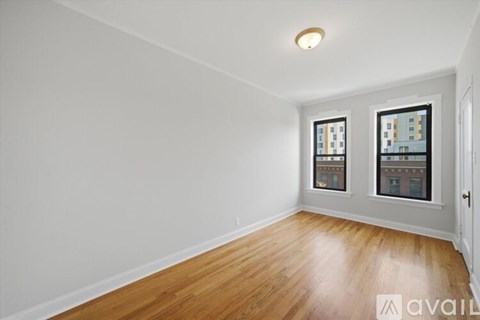 A room with wooden floors and two windows with a view of a building.