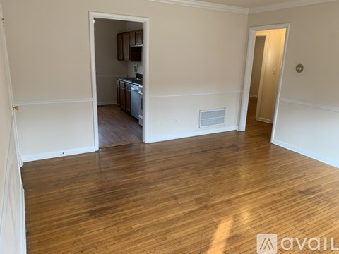 A room with wooden floors and a kitchen visible through the open door.
