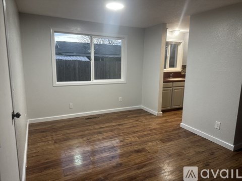 A room with wooden flooring and a window overlooking a fence.