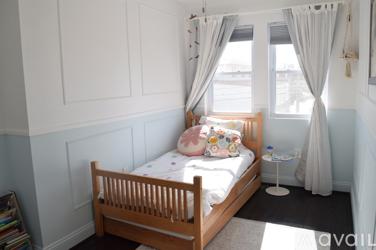 A small child's bedroom with a white bed and a window with curtains.