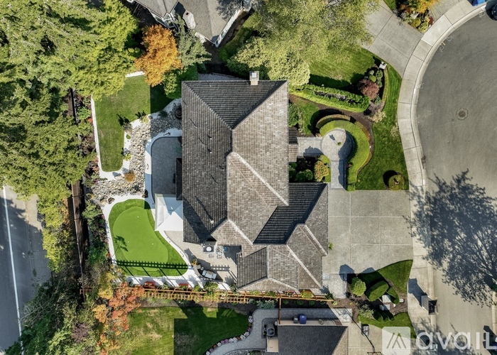 A large house with a grey roof and a white fence is surrounded by a green lawn and trees.