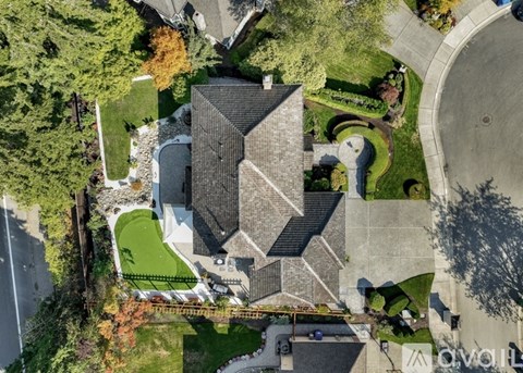 A large house with a grey roof and a white fence is surrounded by a green lawn and trees.
