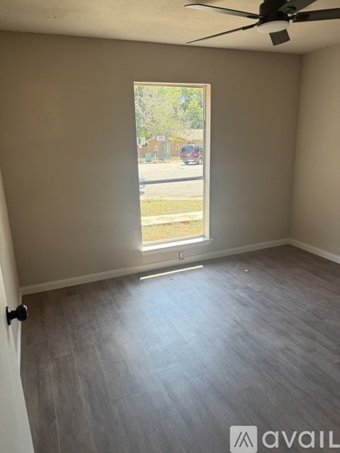A room with a ceiling fan and a window overlooking a street.