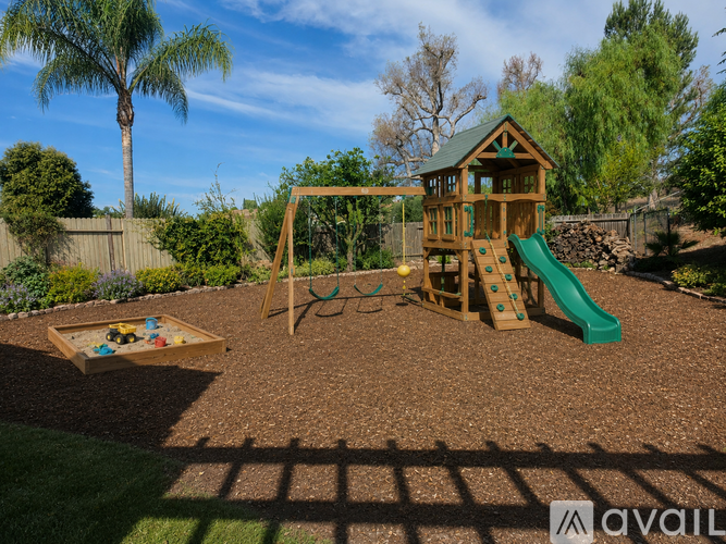 A playground with a green slide and a wooden swing set.