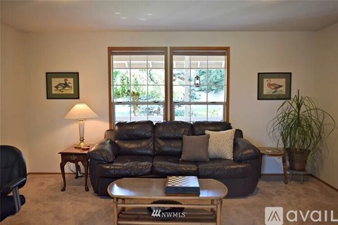 A living room with a black leather couch, a small table with a lamp, and a large window.