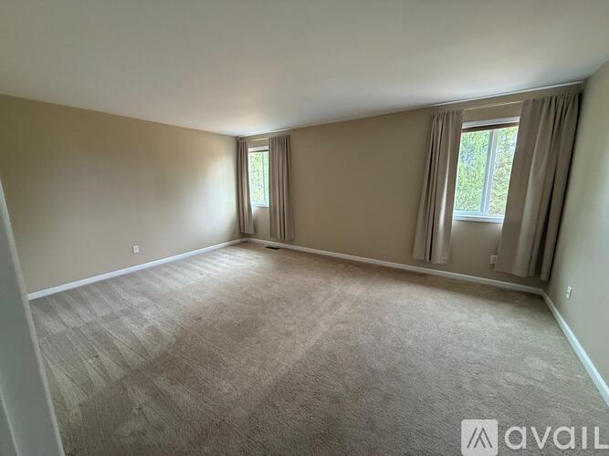 A spacious room with carpeted floor and two windows with curtains.