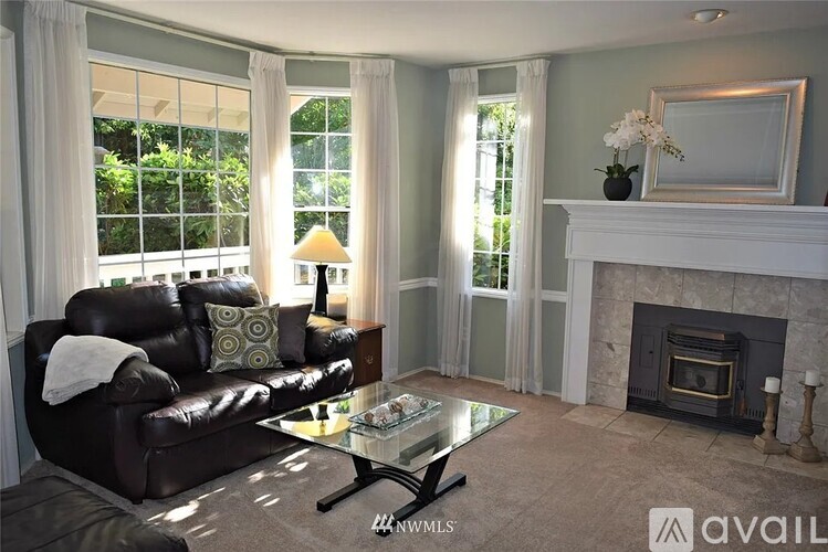 A living room with a black leather couch, a glass coffee table, and a fireplace.