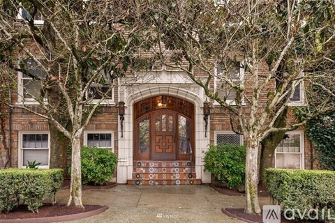A large wooden door is flanked by two trees and a small garden.
