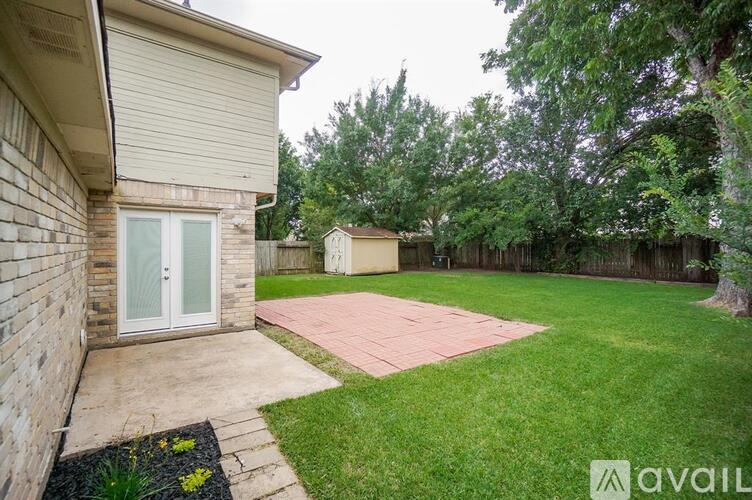 A backyard with a brick building, a green lawn, and a paved walkway.