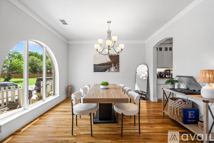 A dining room with a wooden table and chairs, a chandelier, and a view of the backyard through a large window.