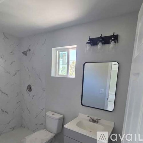 A bathroom with a toilet, sink, mirror, and a window.