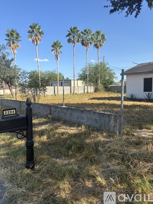 A black mailbox with the number 2201 on it is in front of a grassy area with a white building and palm trees in the background.