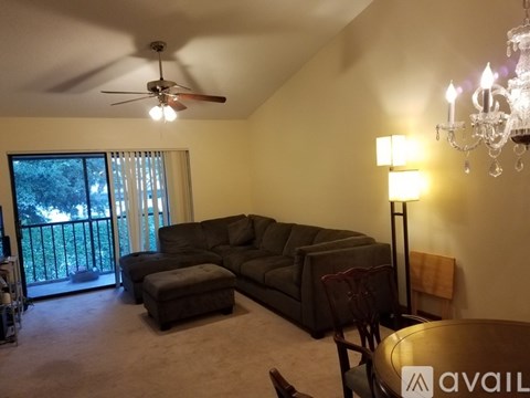 A living room with a grey couch, a brown ottoman, a ceiling fan, and a chandelier.