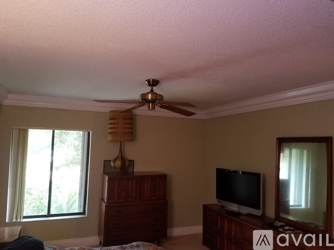 A bedroom with a ceiling fan, a television, and a window.