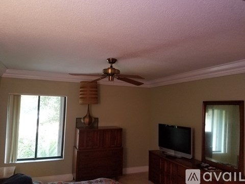 A bedroom with a ceiling fan, a television, and a window.