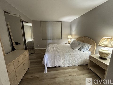 A bedroom with a large bed, a dresser, and a nightstand with a lamp.