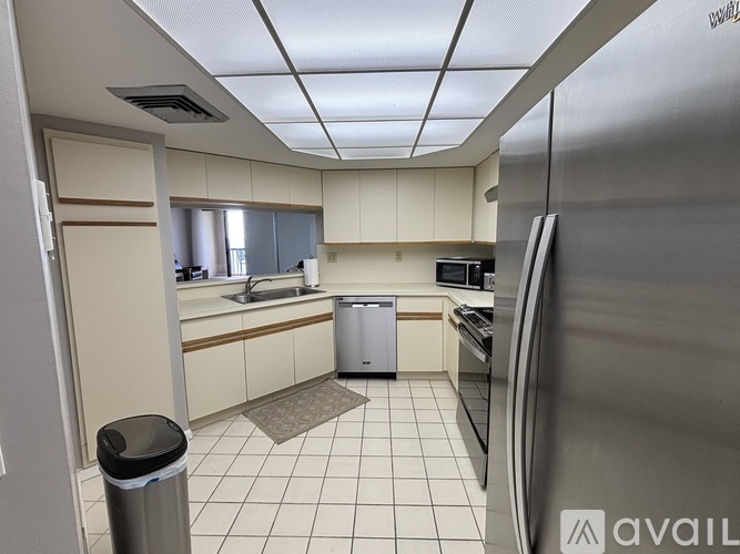 A kitchen with a trash can and a refrigerator.