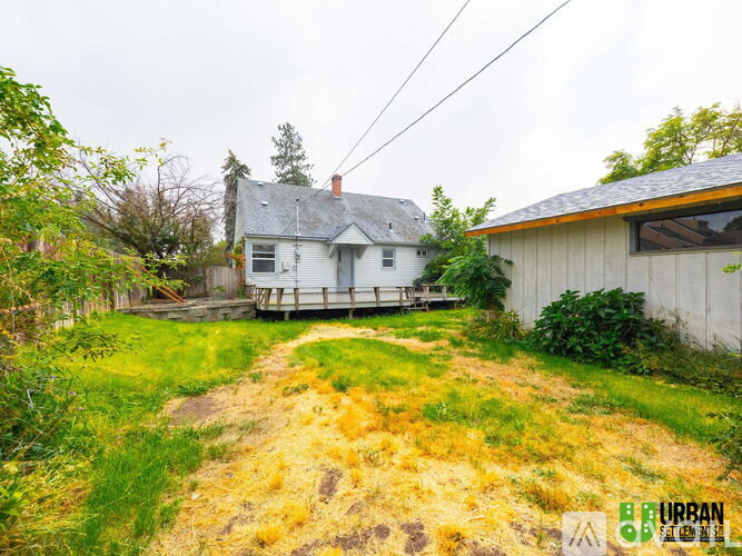 A house with a grey roof and a white exterior is surrounded by a grassy area with a dirt path leading to it.