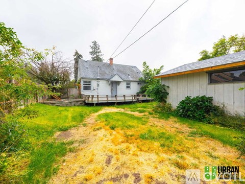 A house with a grey roof and a white exterior is surrounded by a grassy area with a dirt path leading to it.