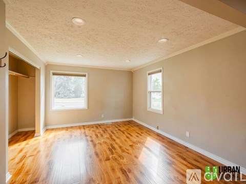 A spacious room with wooden floors and two windows.