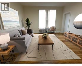 A living room with a grey couch, a wooden coffee table, and a large window with white curtains.