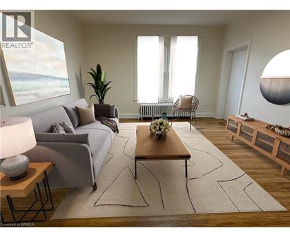 A living room with a grey couch, a wooden coffee table, and a large window with white curtains.