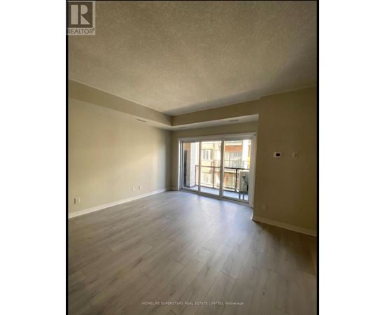 A spacious room with wooden flooring and a sliding glass door leading to a balcony.