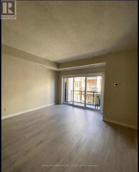 A spacious room with wooden flooring and a sliding glass door leading to a balcony.