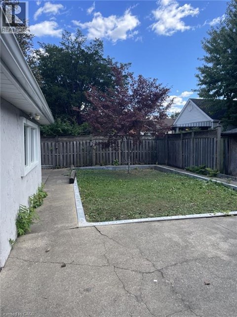 A backyard with a white house, a wooden fence, and a tree.