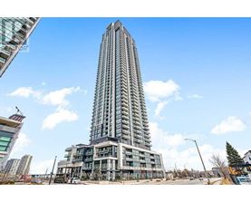 A tall building with many windows stands in front of a blue sky with clouds.