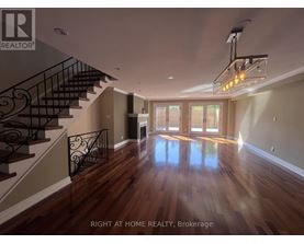 A spacious room with wooden floors and a staircase with a metal railing.