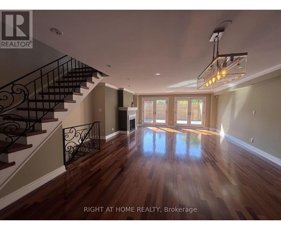A spacious room with wooden floors and a staircase with a metal railing.