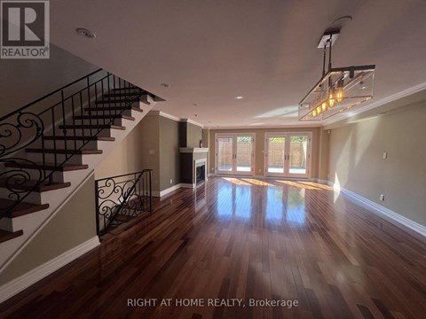 A spacious room with wooden floors and a staircase with a metal railing.