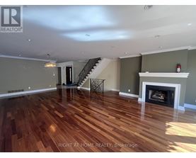 A spacious room with wood flooring and a staircase.