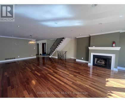 A spacious room with wood flooring and a staircase.