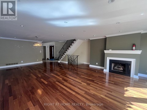 A spacious room with wood flooring and a staircase.