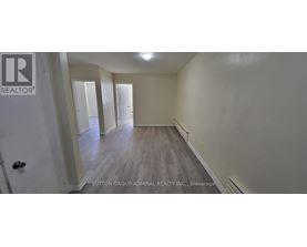 A brokerage sign is on the door of a room with wood flooring and white walls.
