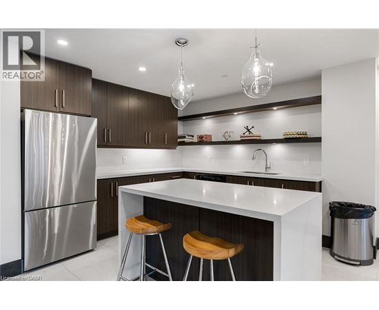 A modern kitchen with a stainless steel refrigerator, bar stools, and a white countertop.