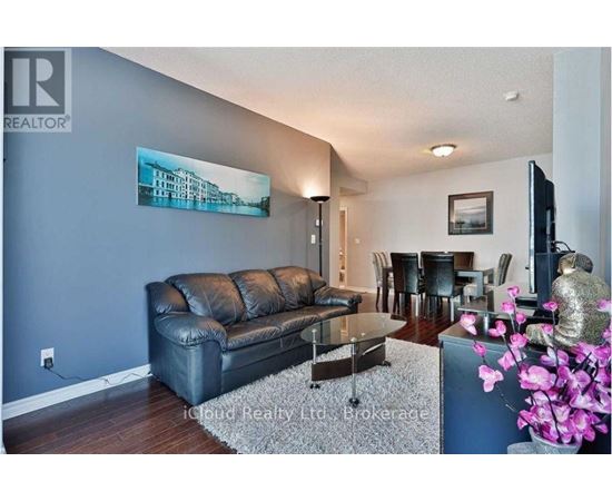 A living room with a black leather couch and a painting on the wall.