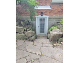 A small white door with a window is surrounded by rocks and plants.