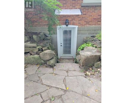A small white door with a window is surrounded by rocks and plants.