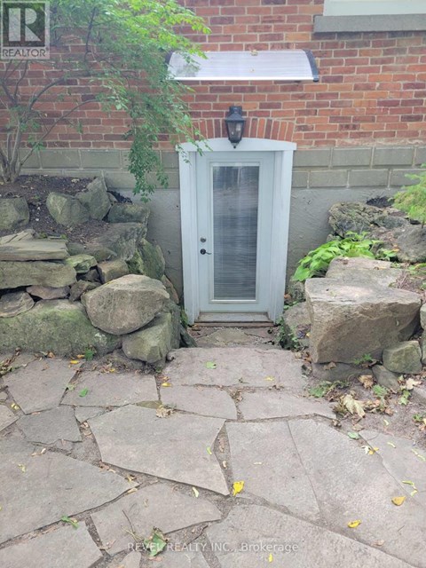 A small white door with a window is surrounded by rocks and plants.