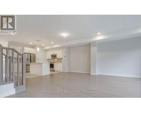 A spacious, empty room with a kitchen area in the background.