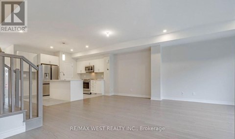 A spacious, empty room with a kitchen area in the background.
