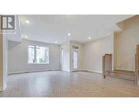 A spacious room with wooden flooring and white walls, with a window on the left side.