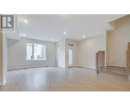 A spacious room with wooden flooring and white walls, with a window on the left side.