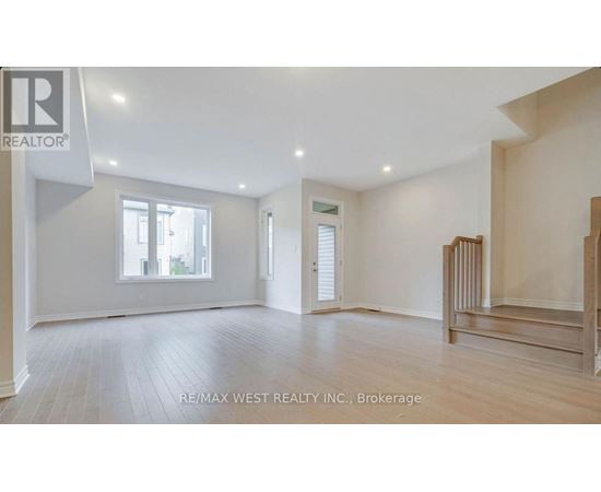 A spacious room with wooden flooring and white walls, with a window on the left side.