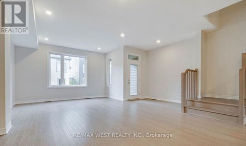 A spacious room with wooden flooring and white walls, with a window on the left side.