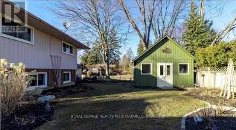 A green house is in the foreground of a photo showing a yard and a pink house.
